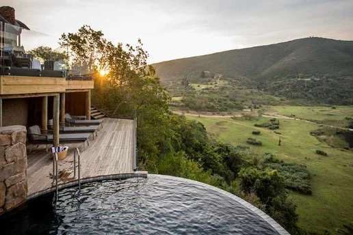 A timber deck and curved plunge pool at Botlierskop, above a green valley in low evening sun