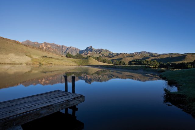 Drakensberg peaks reflected in a still lake at first light, a wooden jetty reaching out from the near bank