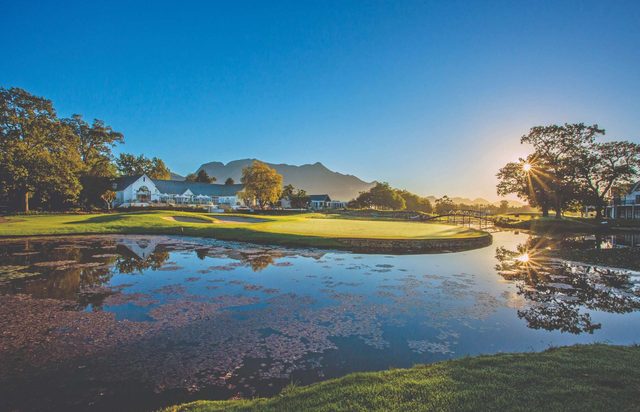 A green at The Links, Fancourt, seen across still water with the mountains behind