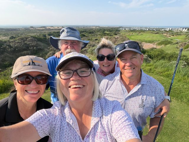 Five guests on a links course, dunes and fairway behind them and the sea on the horizon
